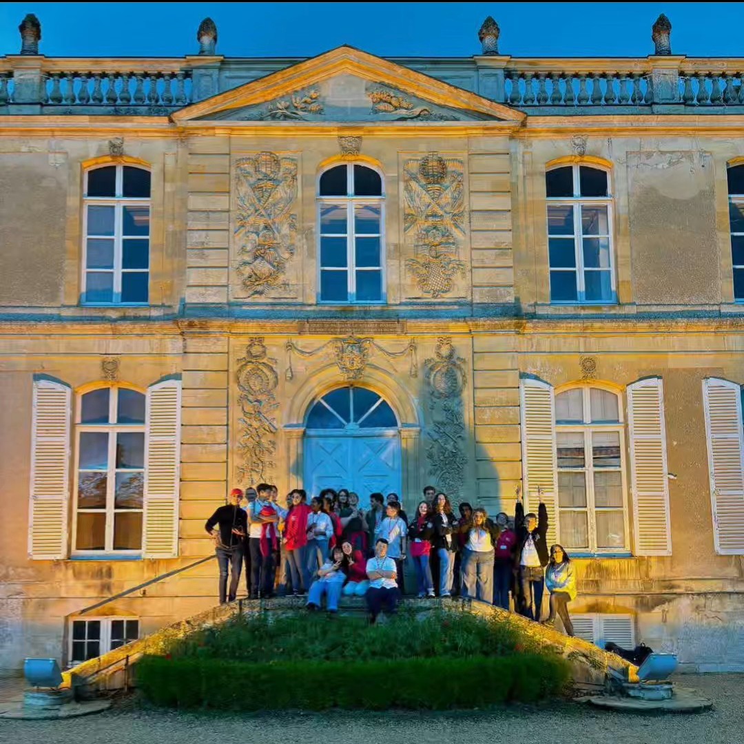 A Grand Building Is Lit Up A Group Of Young People Stand In Front Of It